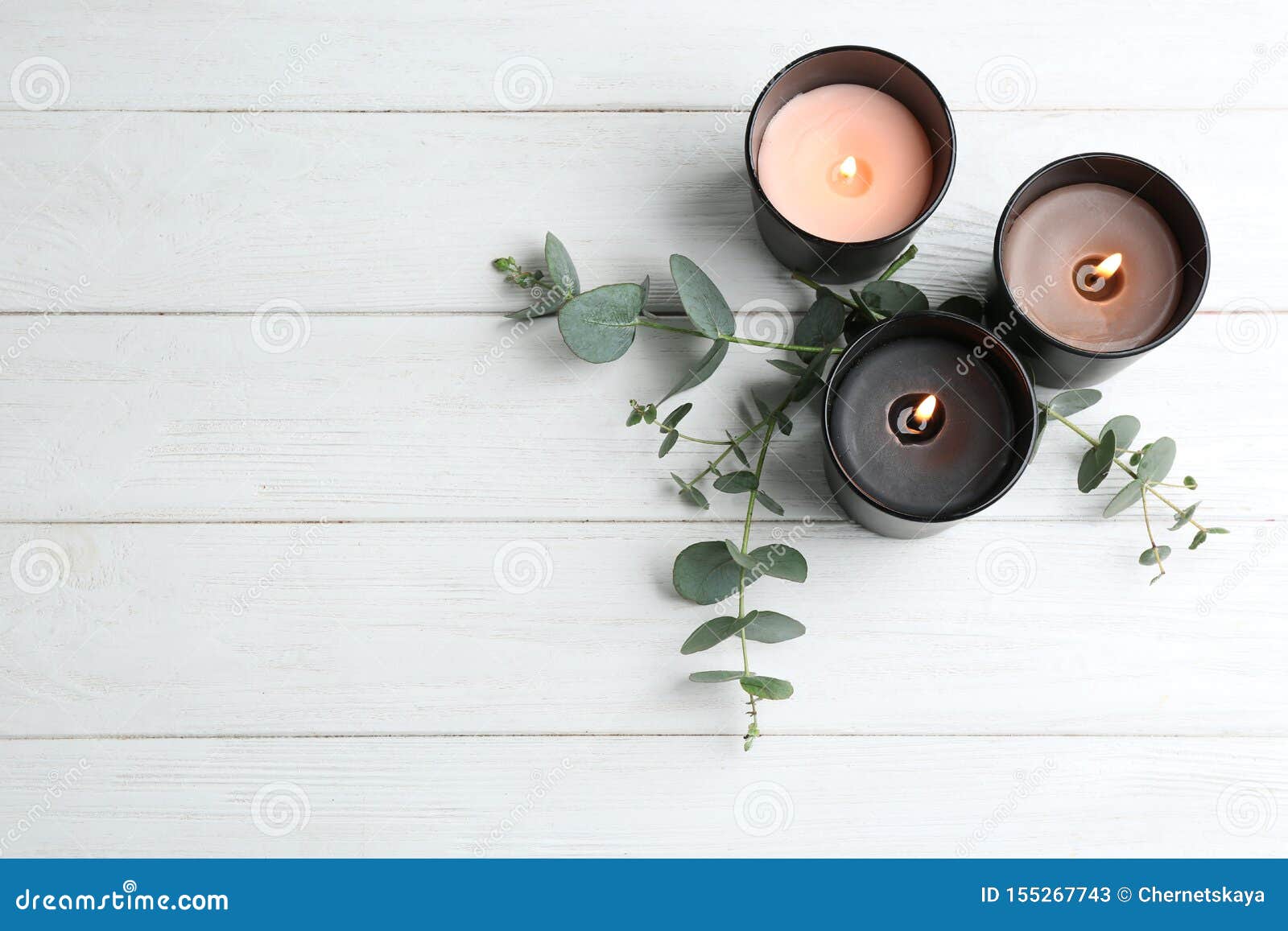 burning candles and green branches on white wooden table, flat lay.