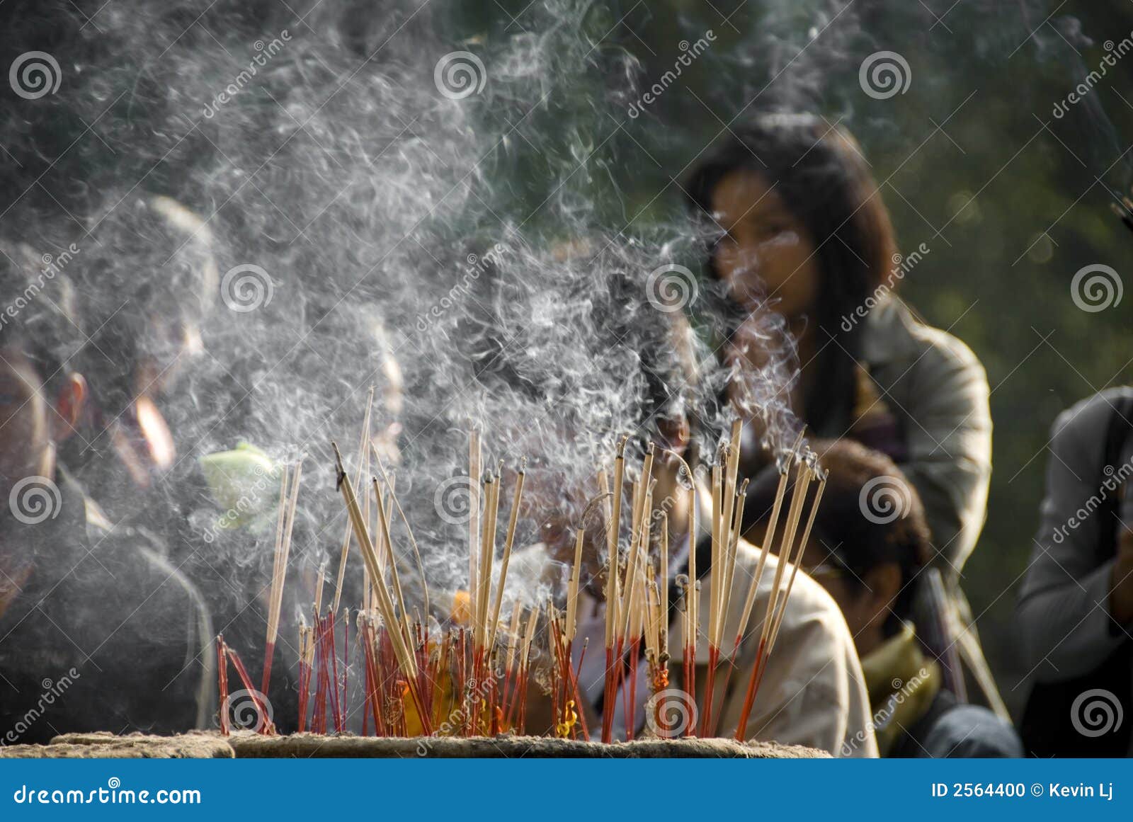 Burning do incenso. Muitos incense a vara em um urn em um santuário budista tailandês que queima-se com lotes do fumo e dos povos fora de foco no fundo