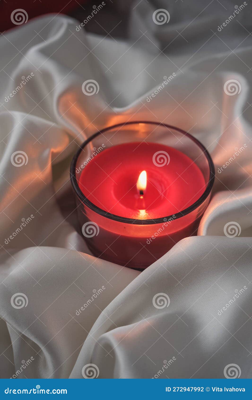 Burning Red Candle in a Glass Bowl on a White Silk Background Stock