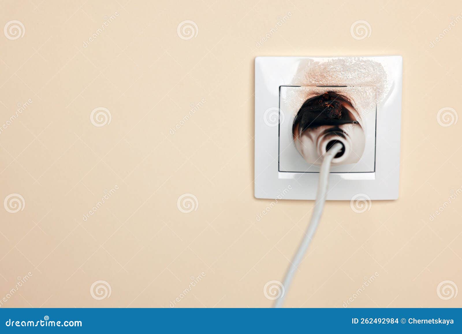 Burnt Plug in Power Socket on Beige Wall, Space for Text. Electrical Short Circuit Stock Photo
