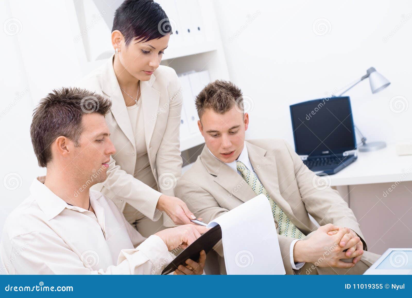 Three young businesspeople having business meeting, looking at document and smiling.