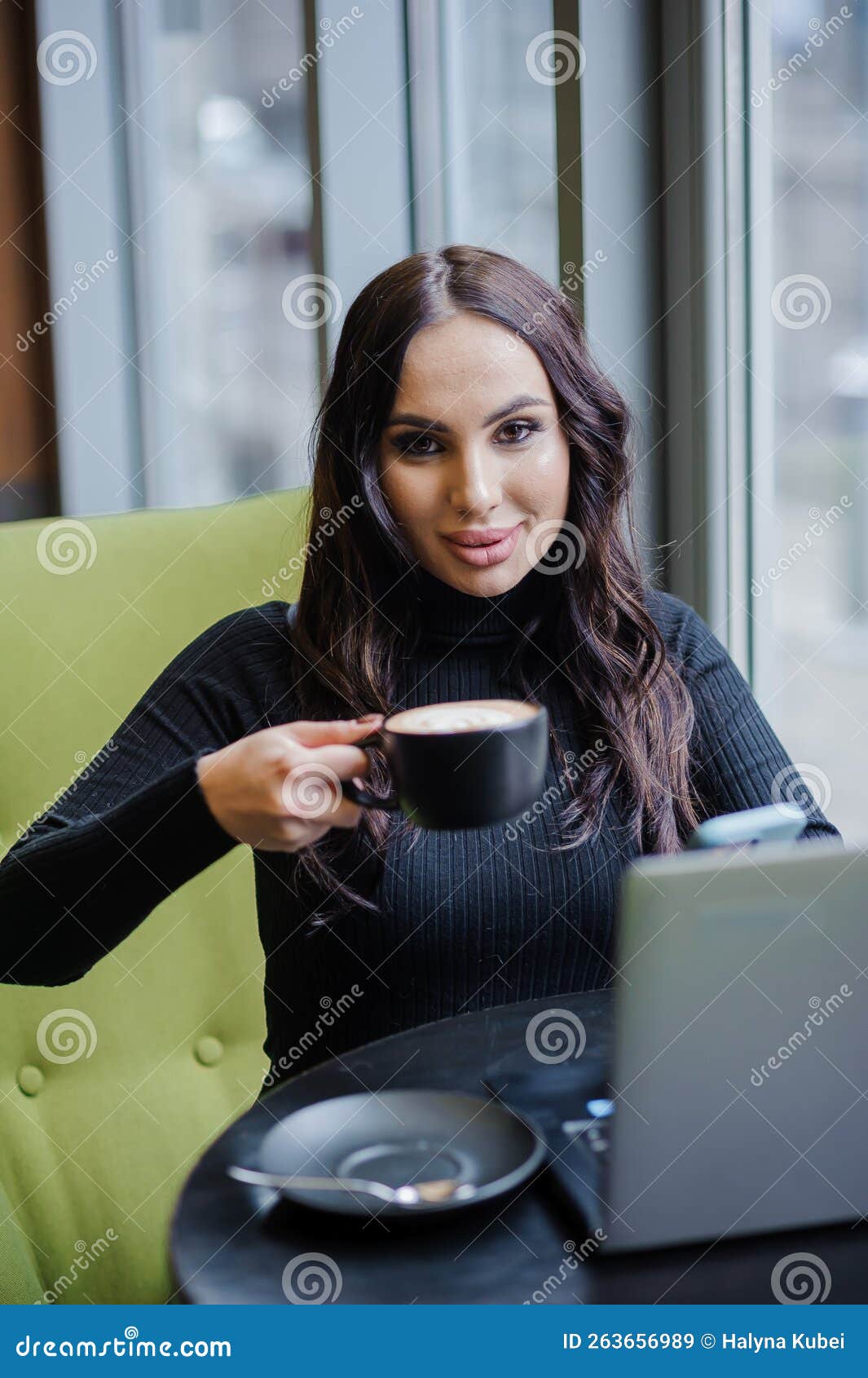 A Business Woman Is Sitting At A Table In The Office Talking On The Phone Working On A Laptop