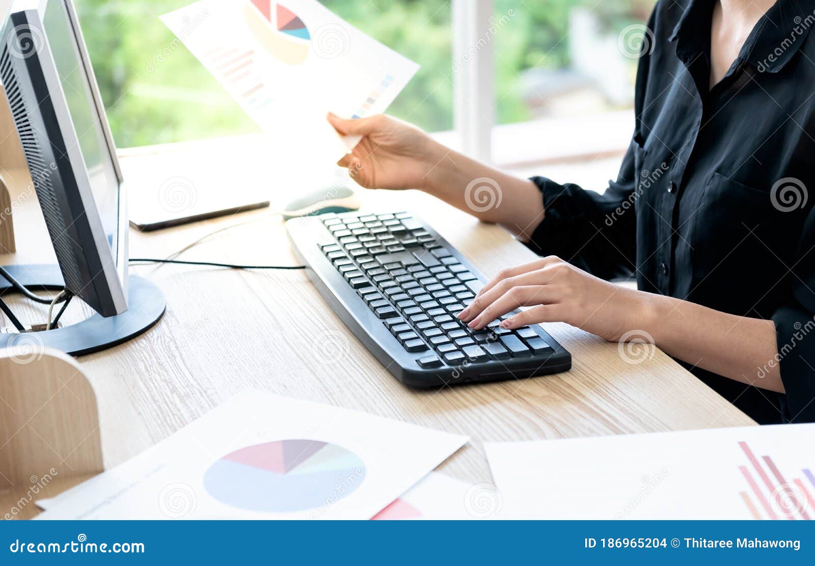 business woman using computer to analyze performance data from paper graph reports