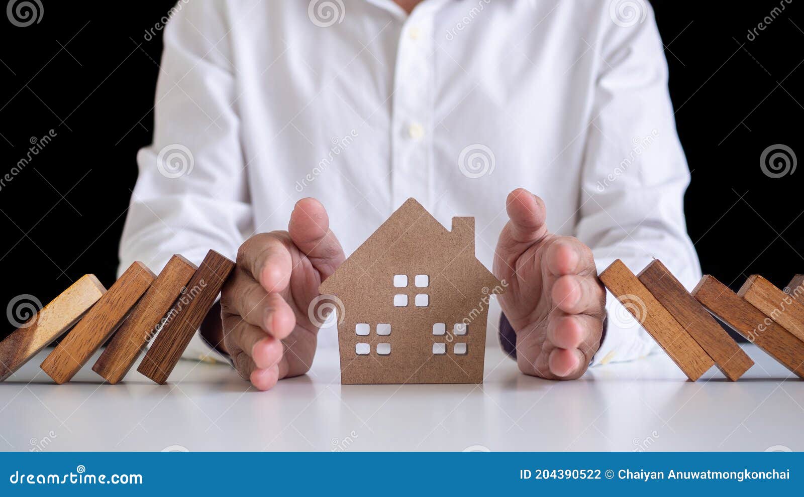 a businessman or a butler using his hand to protect the house from the falling of a wooden domino. home protection insurance for s