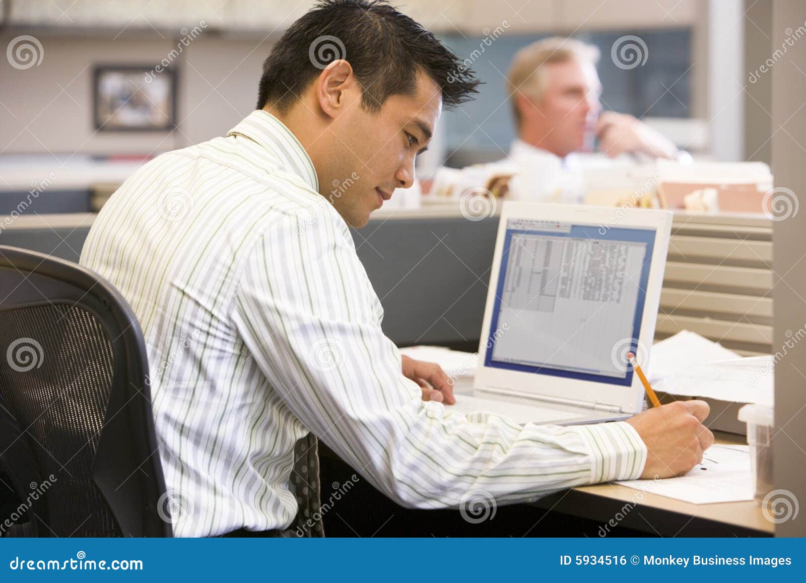 businessman in cubicle with laptop writing