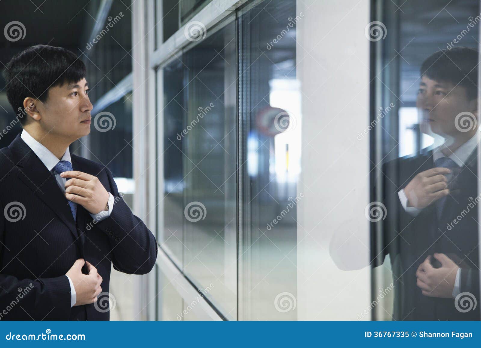 Businessman looking at his reflection and adjusting his tie