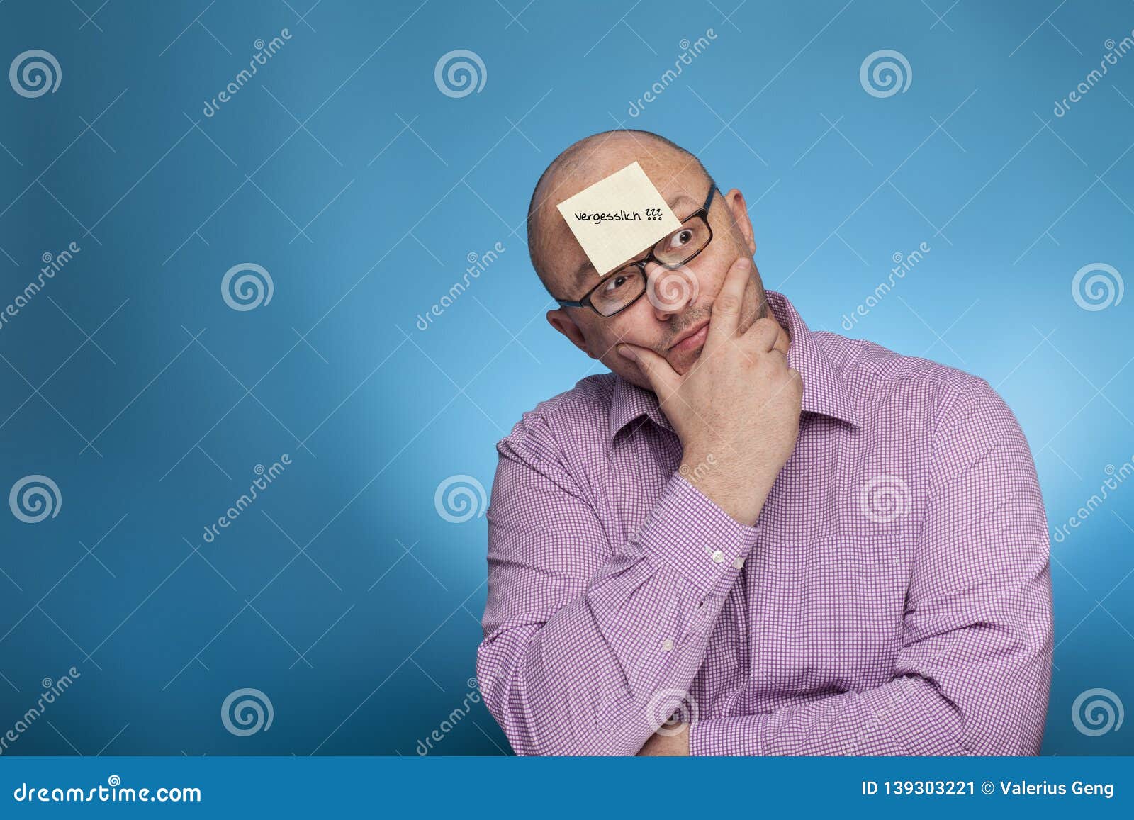 a businessman in a piked shirt has a blank post it on the forehead with german word vergesslich