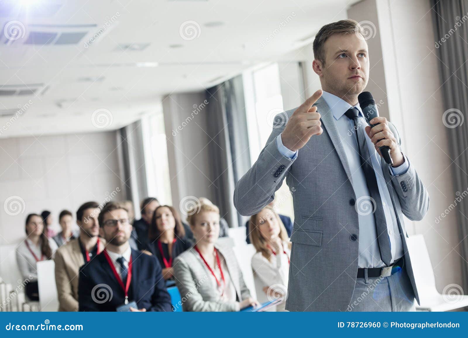 Businessman Pointing while Speaking through Microphone during Seminar