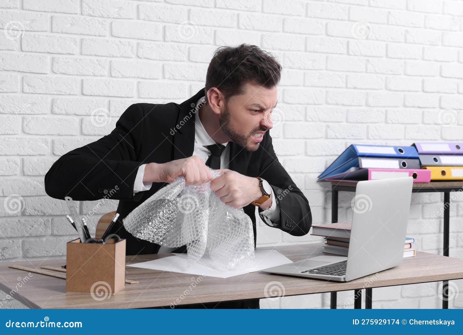 Businessman Popping Bubble Wrap at Workplace in Office. Stress Relief
