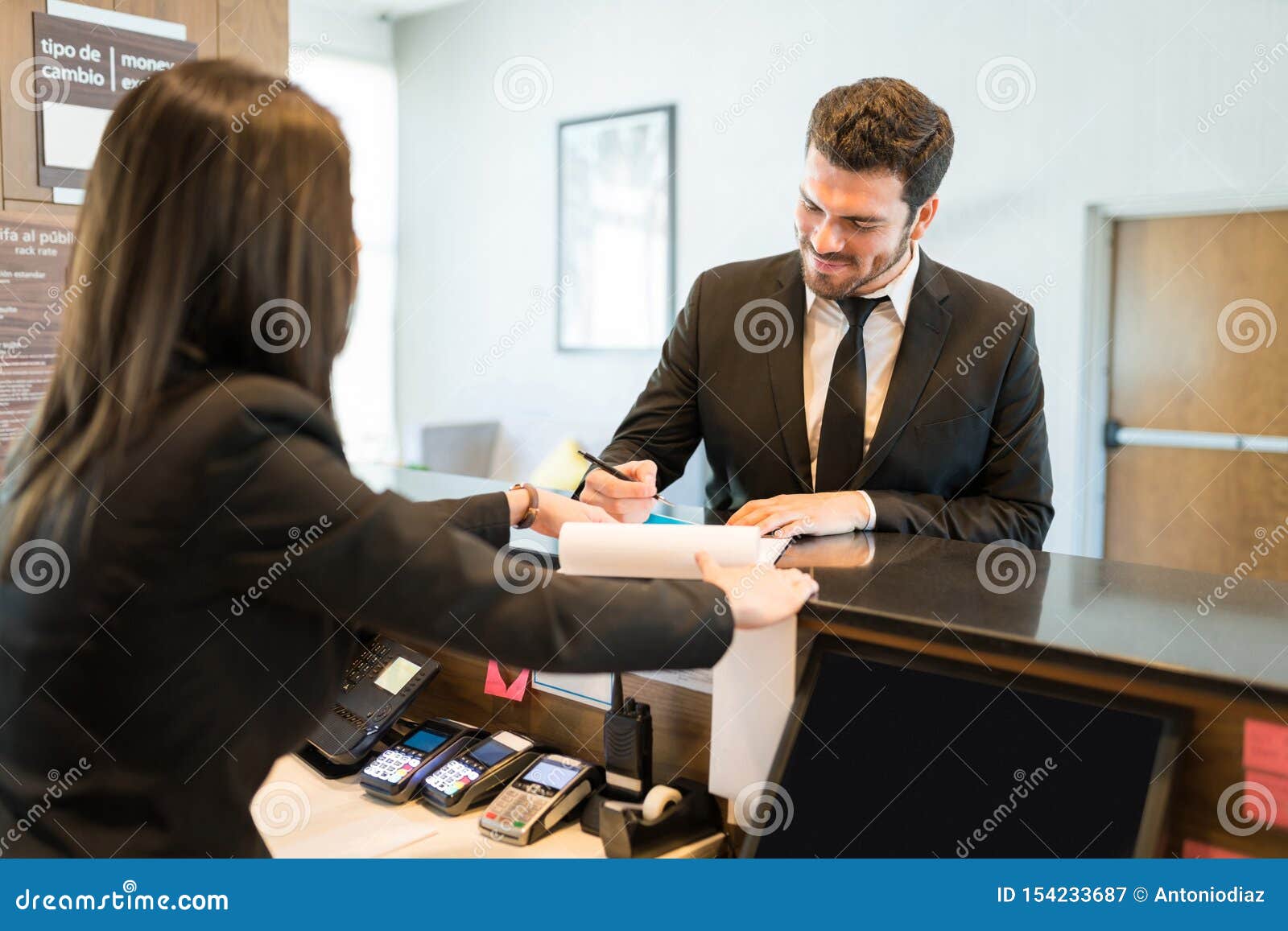 Businessman Signing Document With Clerk At Front Desk Stock Image