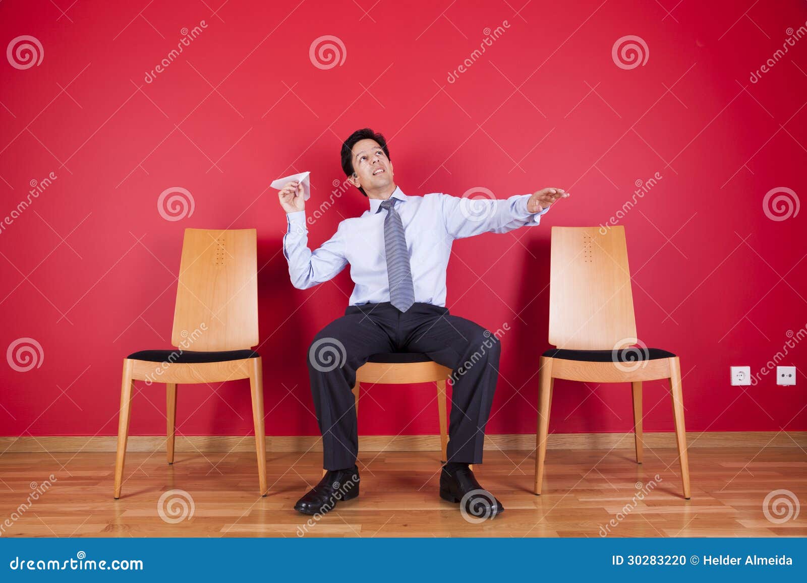 Businessman trowing paper planes. Businessman sited next to a red wall trowing paper planes