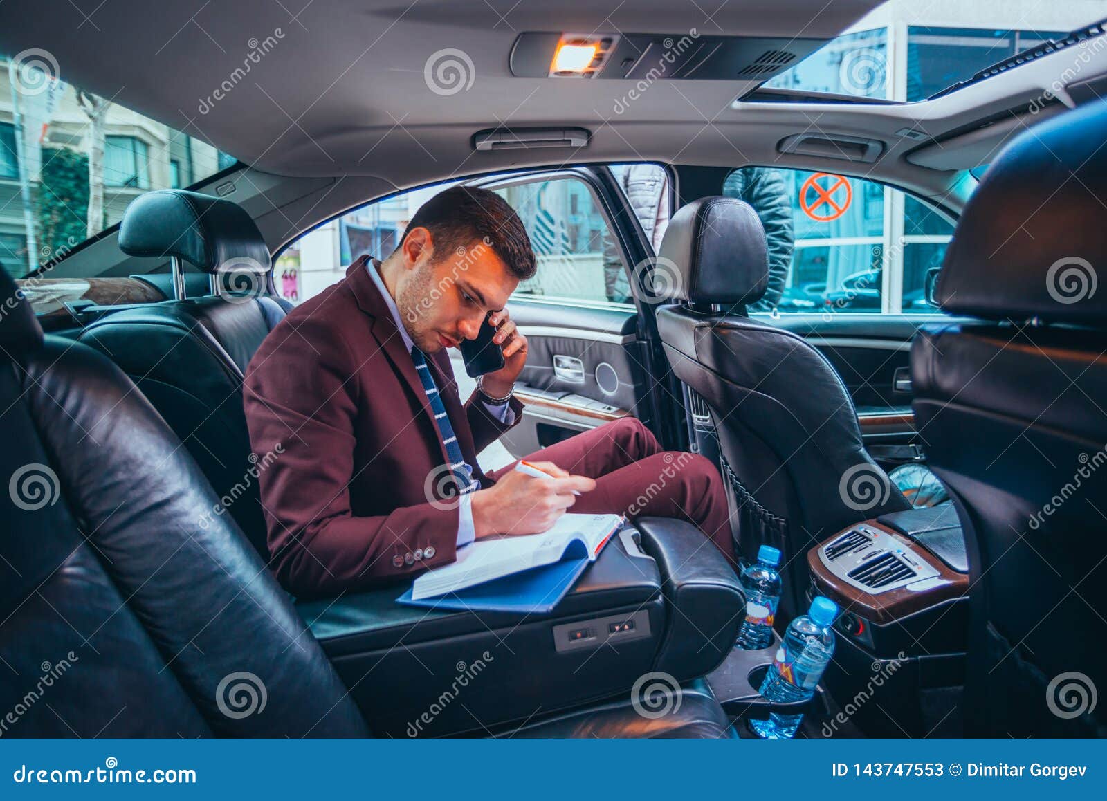 businessman sitting in a limo while talking on his phone reading his notes and planning his day