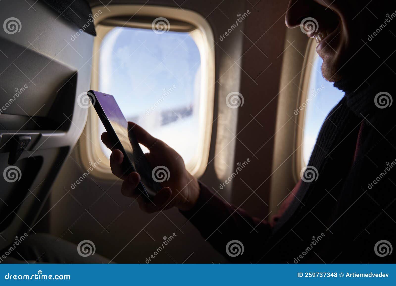 businessman sitting next to airplane window and using smartphone. depersonalized man fly on plane and reading with phone