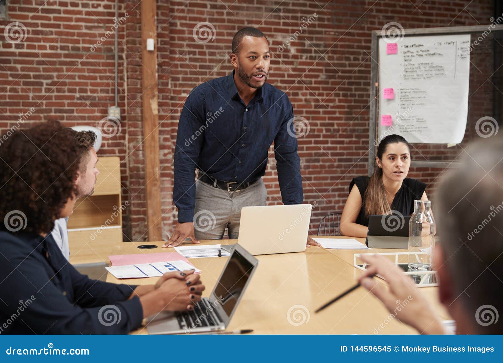 Businessman Standing and Leading Office Meeting Around Table Stock