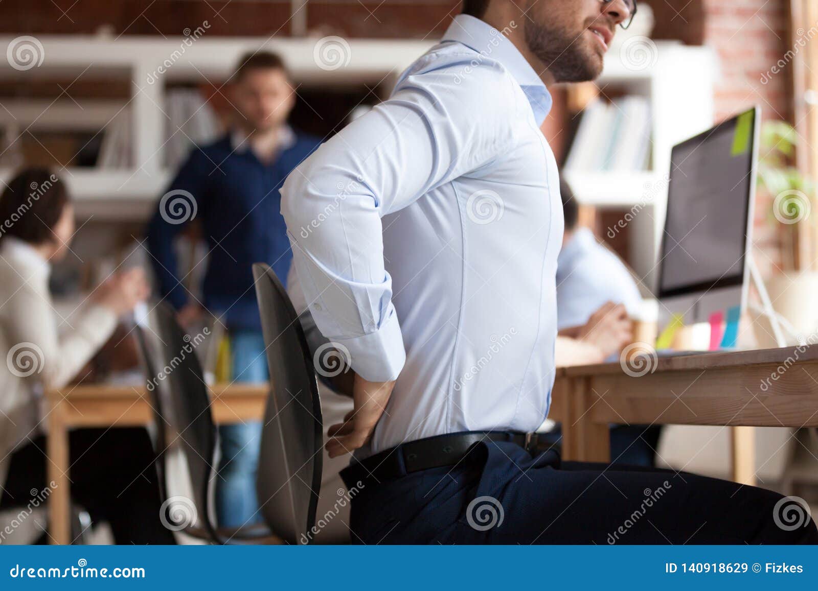 Businessman Suffers From Lower Back Pain Sitting In Shared Office
