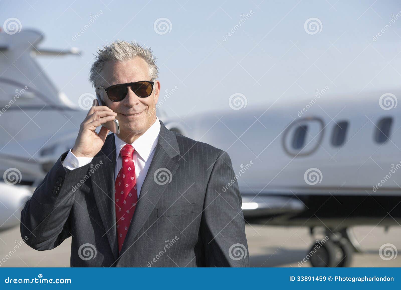 businessman using cell phone with private jet in background