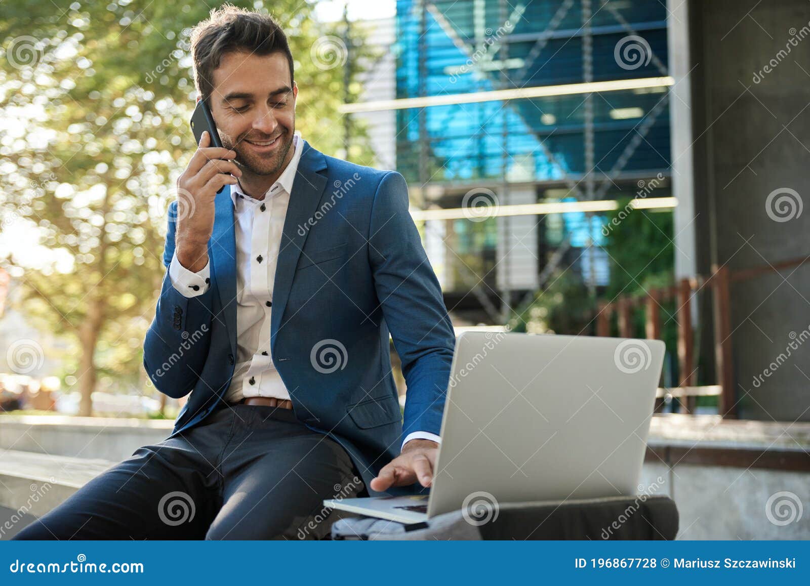 businessman using a laptop outside and talking on his cellphone