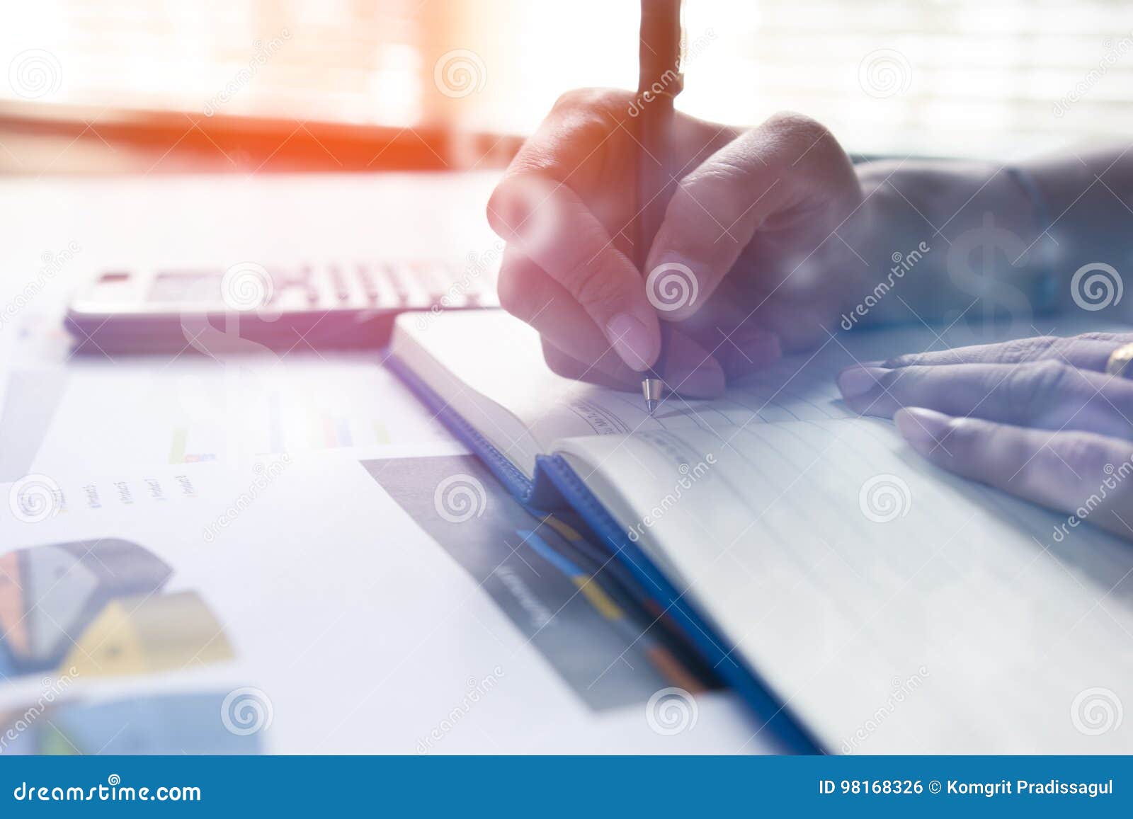 businessman writing on notebook on wooden table, people are recording accounting data calculated from a calculator.