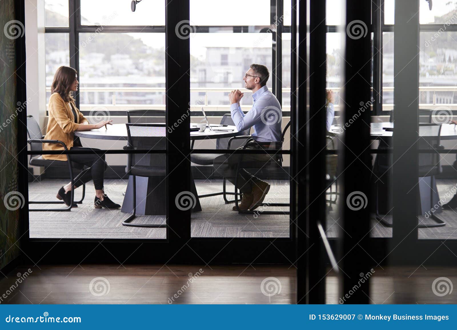 a businessman and young woman meeting for a job interview, full length, seen through glass wall