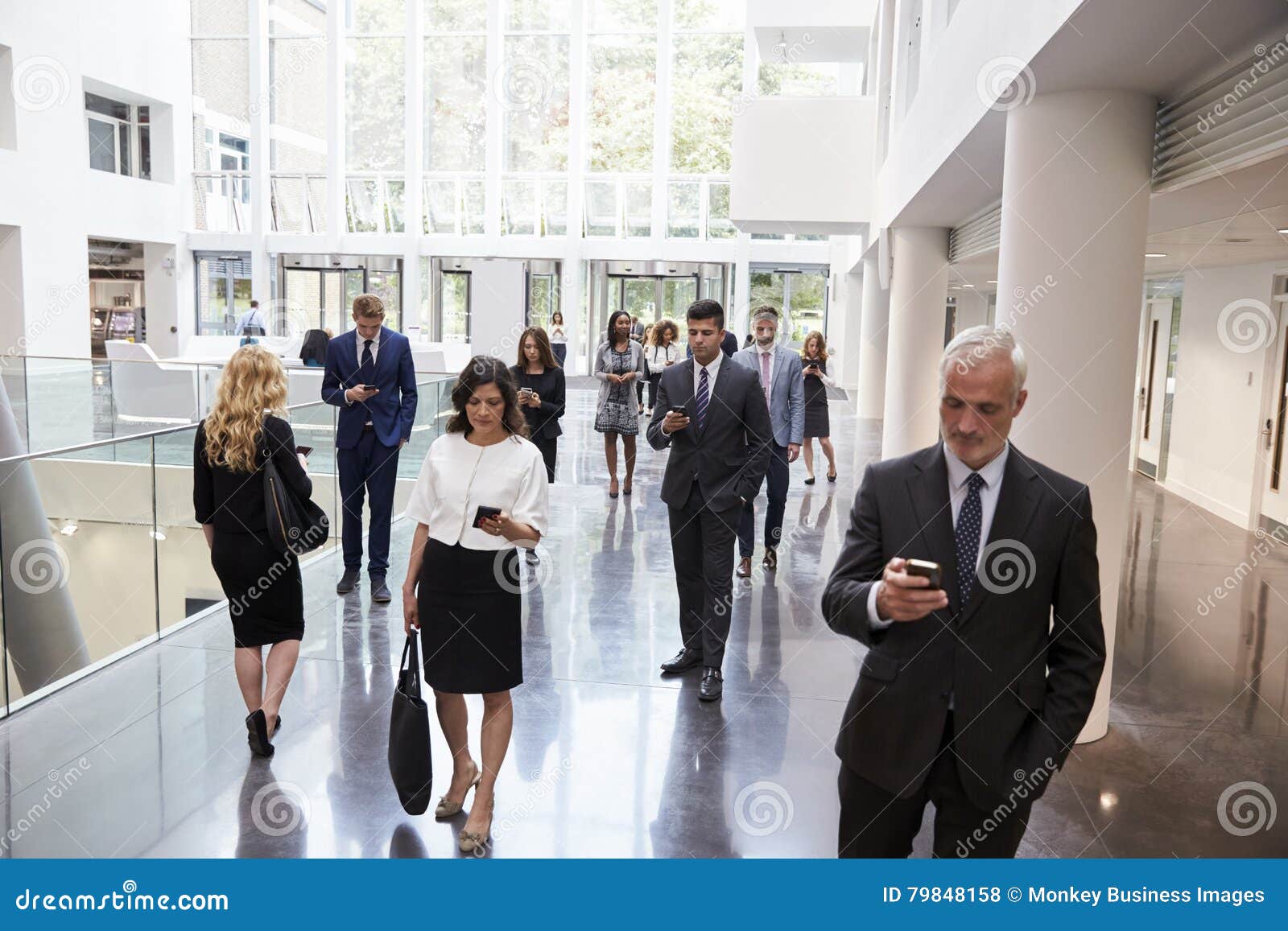 businesspeople using technology in busy lobby area of office