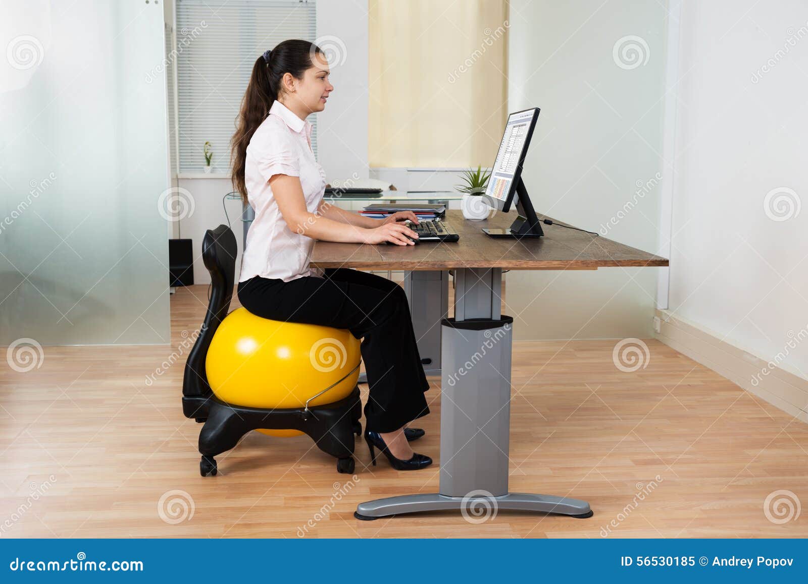 Businesswoman Sitting On Fitness Ball With Computer At Desk Stock