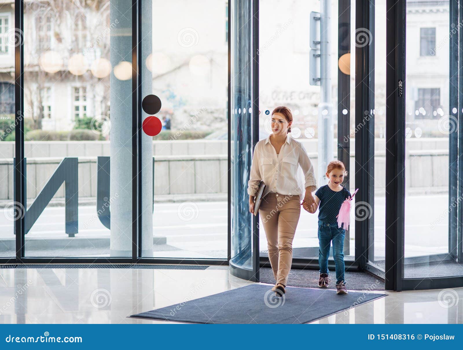 a businesswoman with small daughter entering office building, walking.