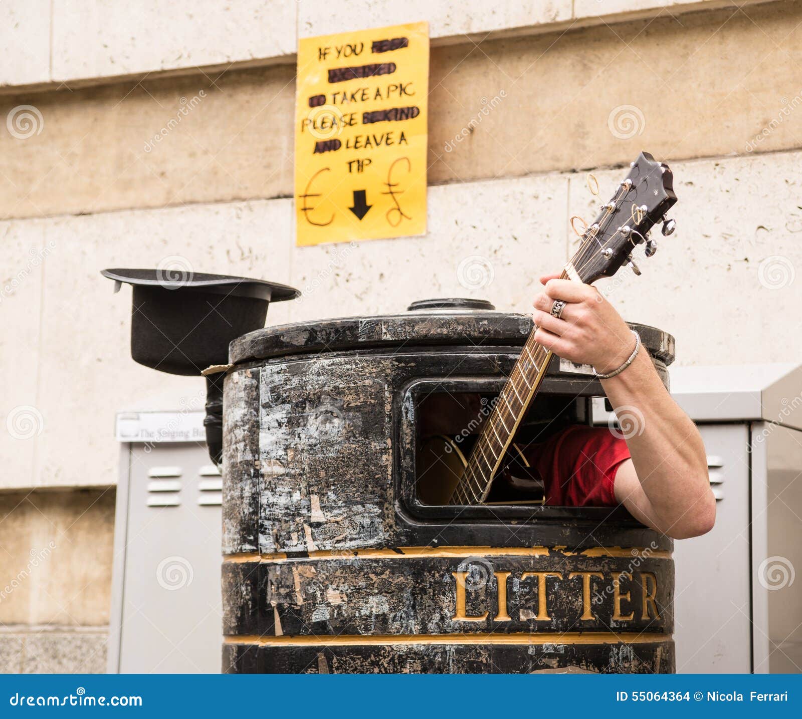busker singing and playing guitar inside a rubbish bin