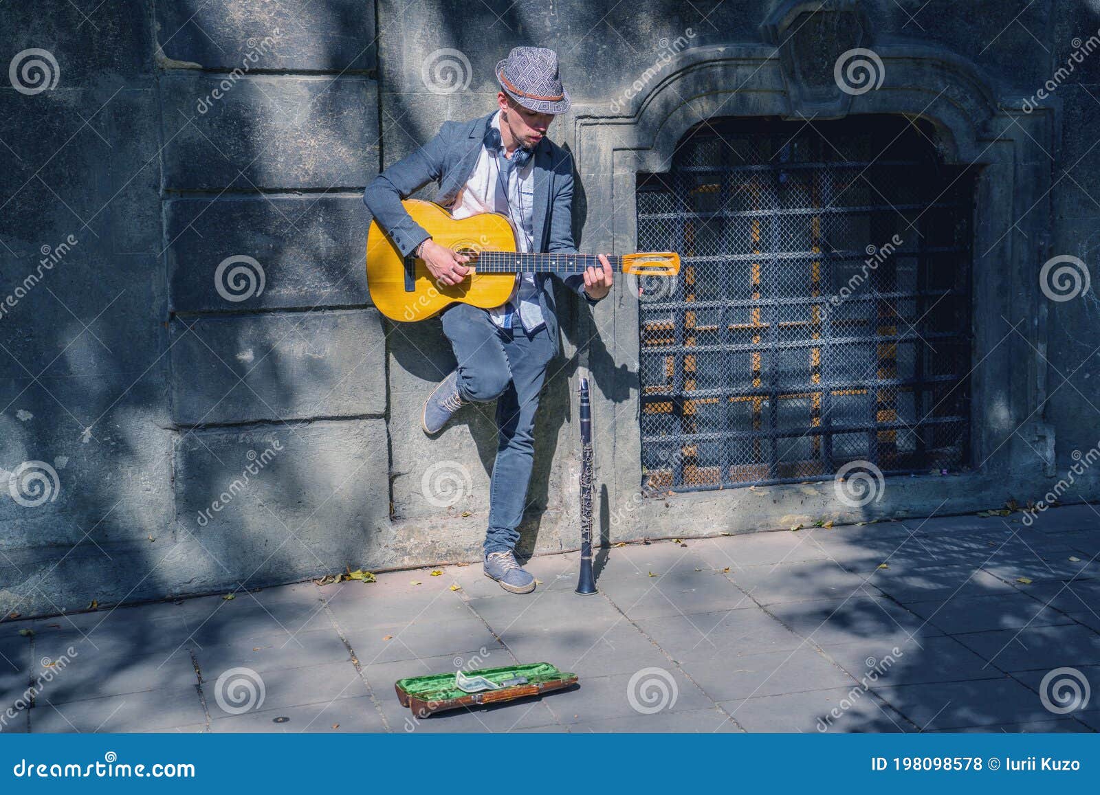 a busker street musician playing music with guitar on a city sidewalk