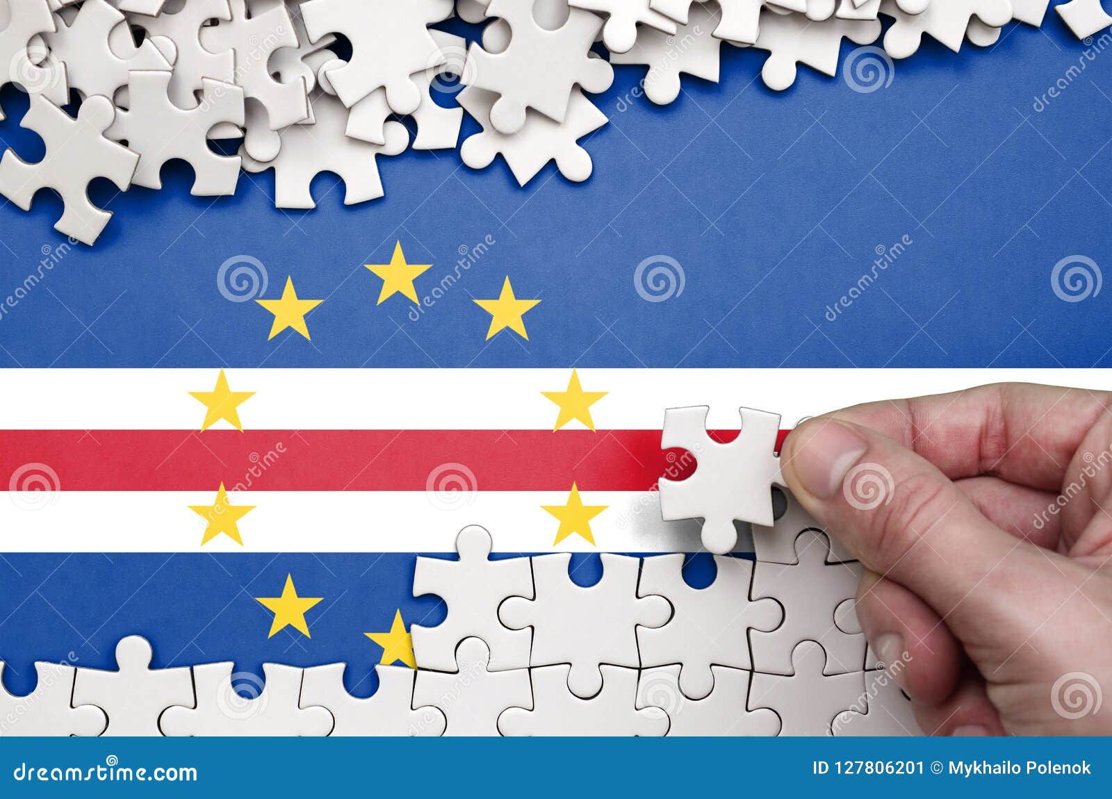 cabo verde flag is depicted on a table on which the human hand folds a puzzle of white color