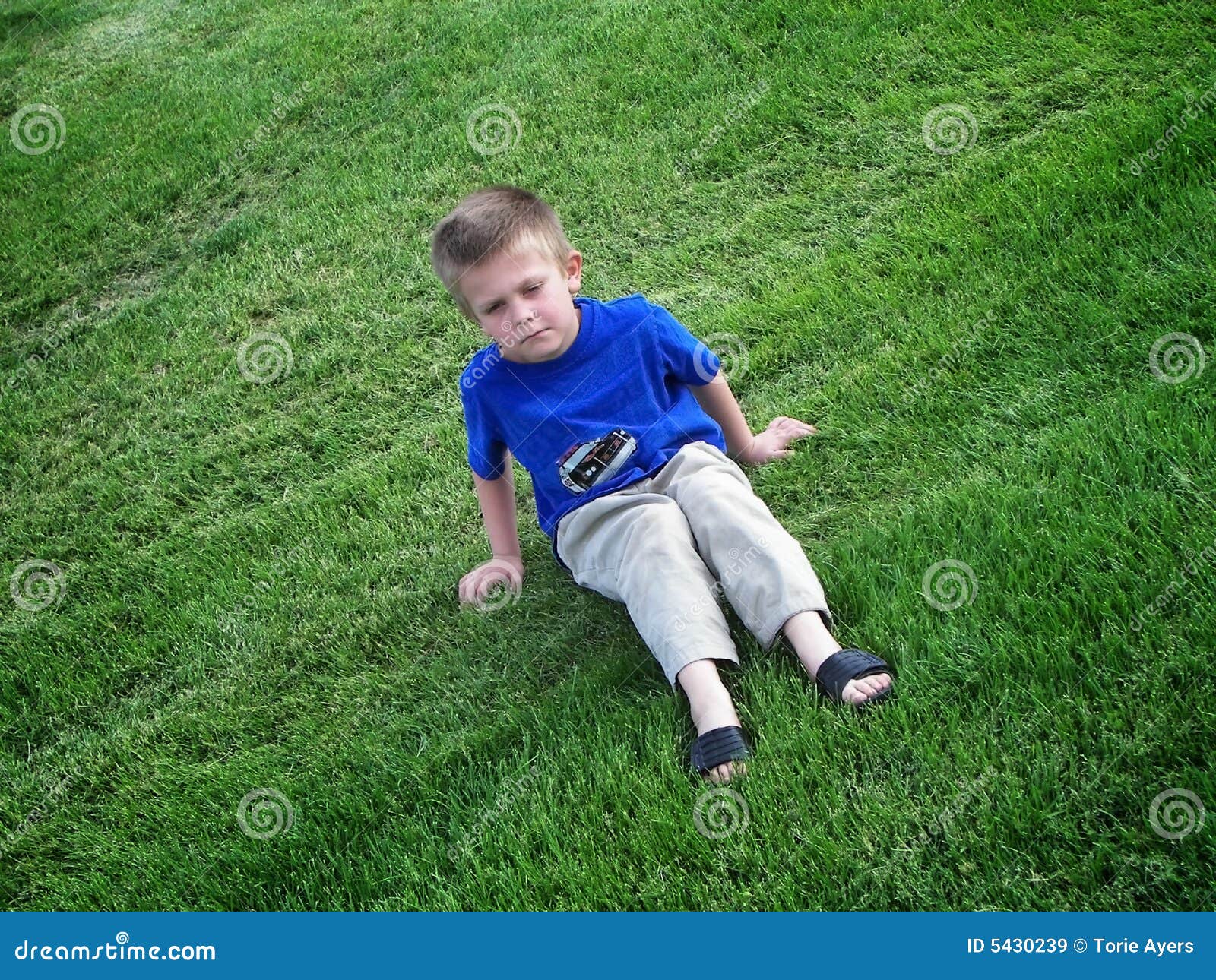 Cabrito gruñón en hierba. Un muchacho gruñón que se sienta y que pone mala cara en un campo de la hierba