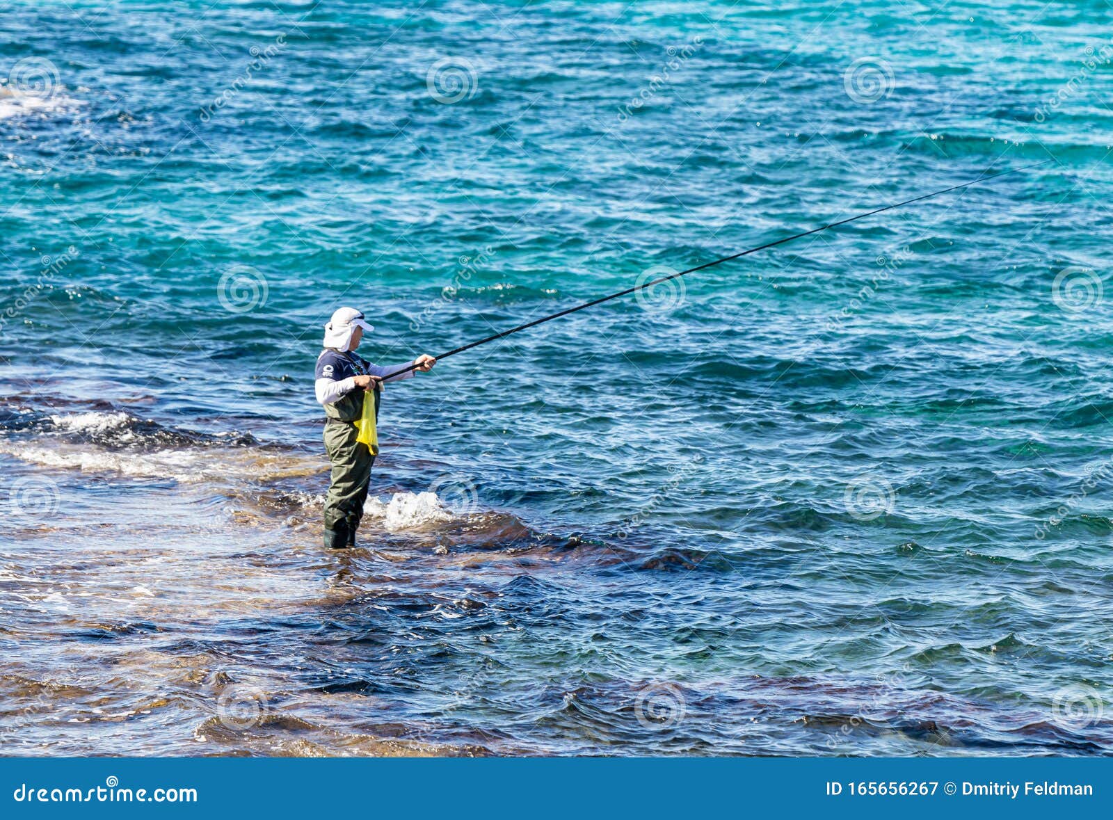 Person fishing on cliff catches starfish by calm sea at sunset