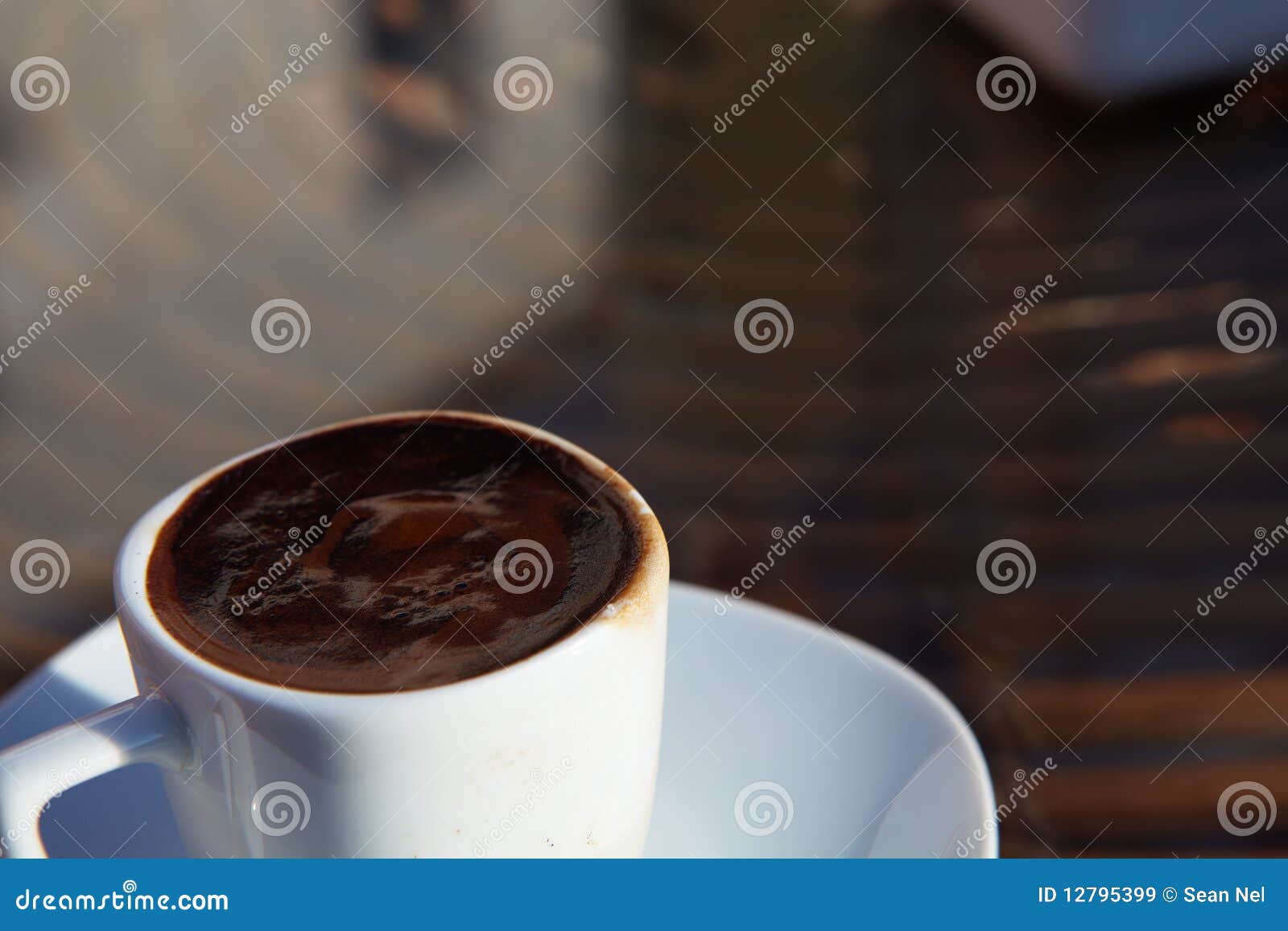 Café turco real em um copo branco pequeno da porcelana em uma tabela em um café ao ar livre em um dia ensolarado. DOF muito raso, foco na borda do copo e espuma.