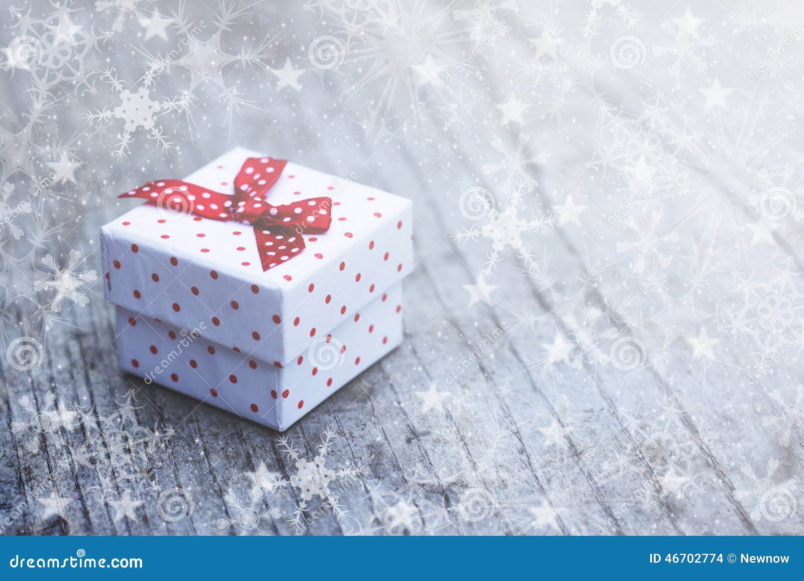 Caja de regalo blanca con los puntos rojos colocados en fondo de madera con efecto de los copos de nieve