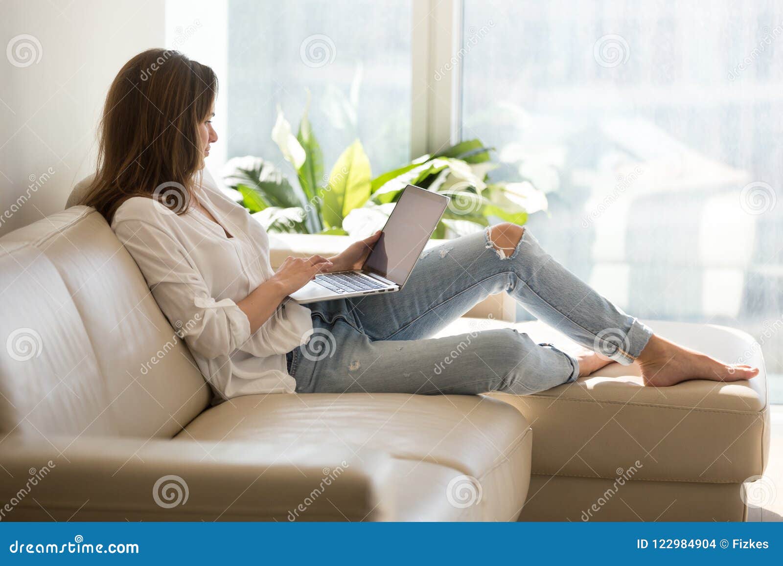 happy female browsing internet sitting on sofa at home