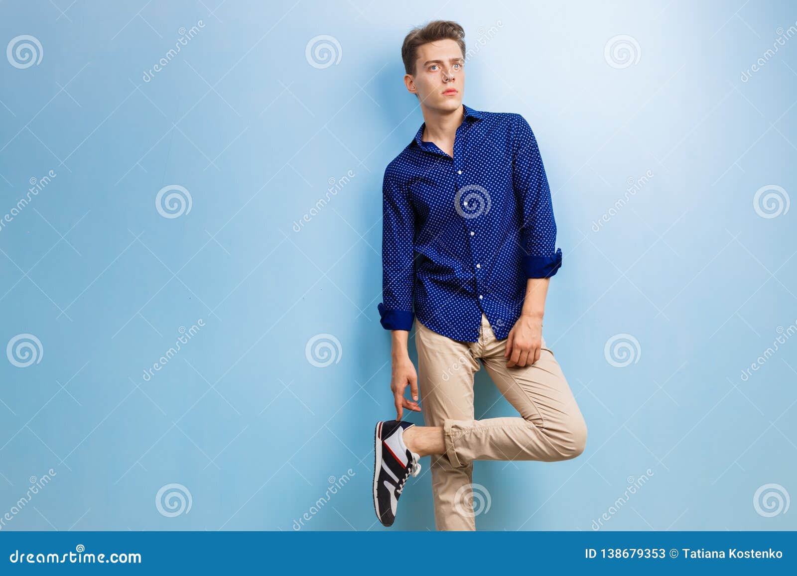 Zdjęcie Stock: Young man reading outside in New York City, wearing light  purple, long sleeve shirt, beige pants, black shoes, standing by silver  metal wall on street, hands holding blue tablet computer,