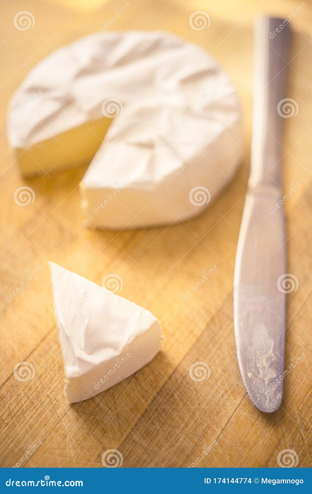 Camembert Cheese with a Triangular Slice and a Knife on a Wooden Board