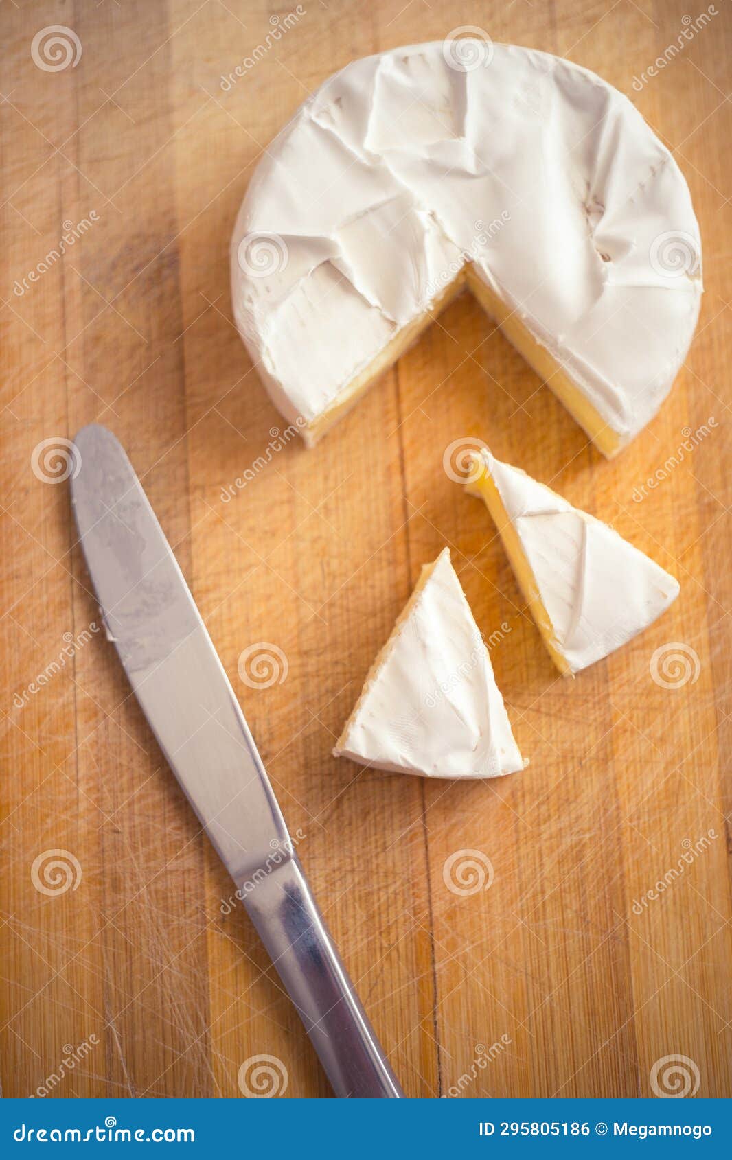 Camembert Cheese with a Triangular Slice and a Knife on a Wooden Board