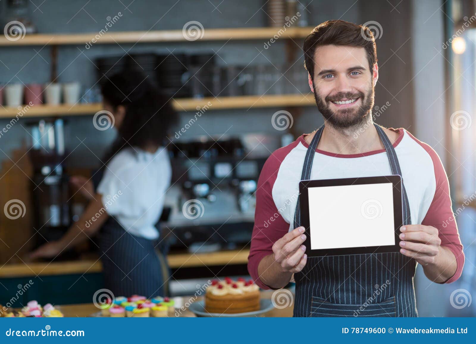 Ritratto del cameriere sorridente che mostra compressa digitale al contatore nel cafÃ©