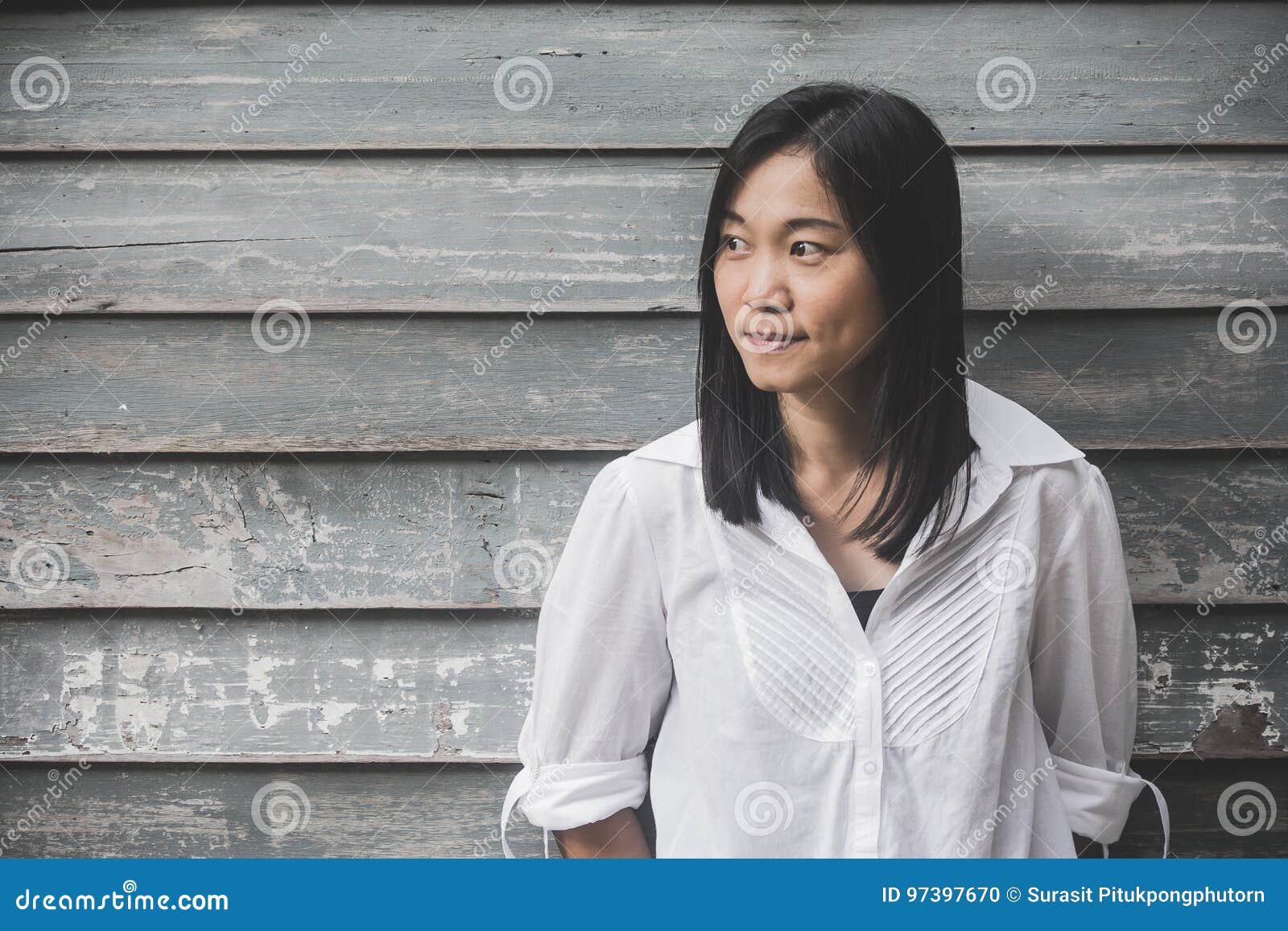 Camicia bianca della donna della foto del tiro di usura asiatica del ritratto e guardare lateralmente con il fondo di legno della. Camicia bianca della donna della foto del tiro di usura asiatica del ritratto e guardare lateralmente con effetto d'annata del filtro dal fondo di legno della parete