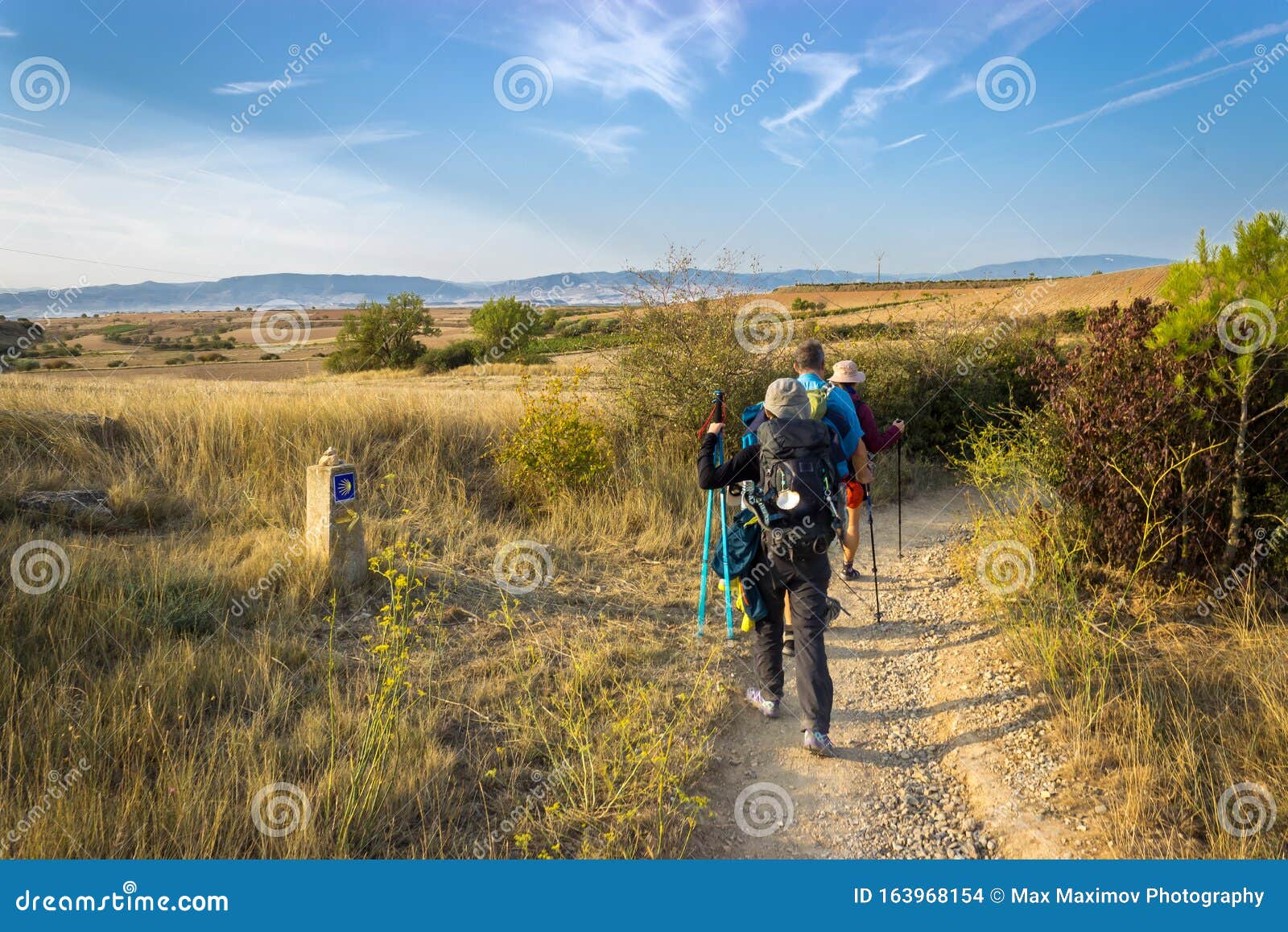 camino de santiago, spain - pilgrims hiking through countryside past a waymark post along the way of st james camino de santiago