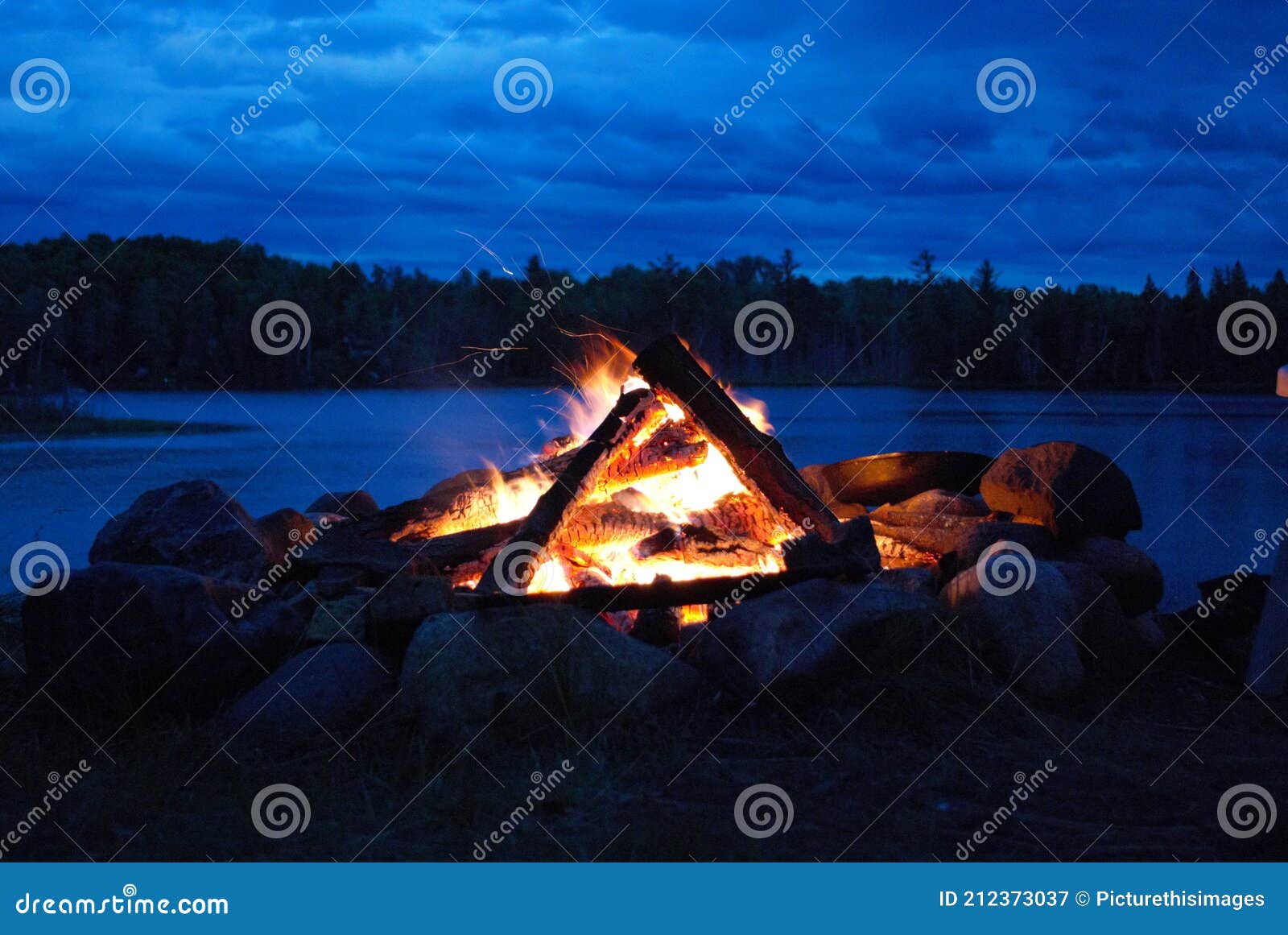 camp fire burning in a fire pit next to the lake