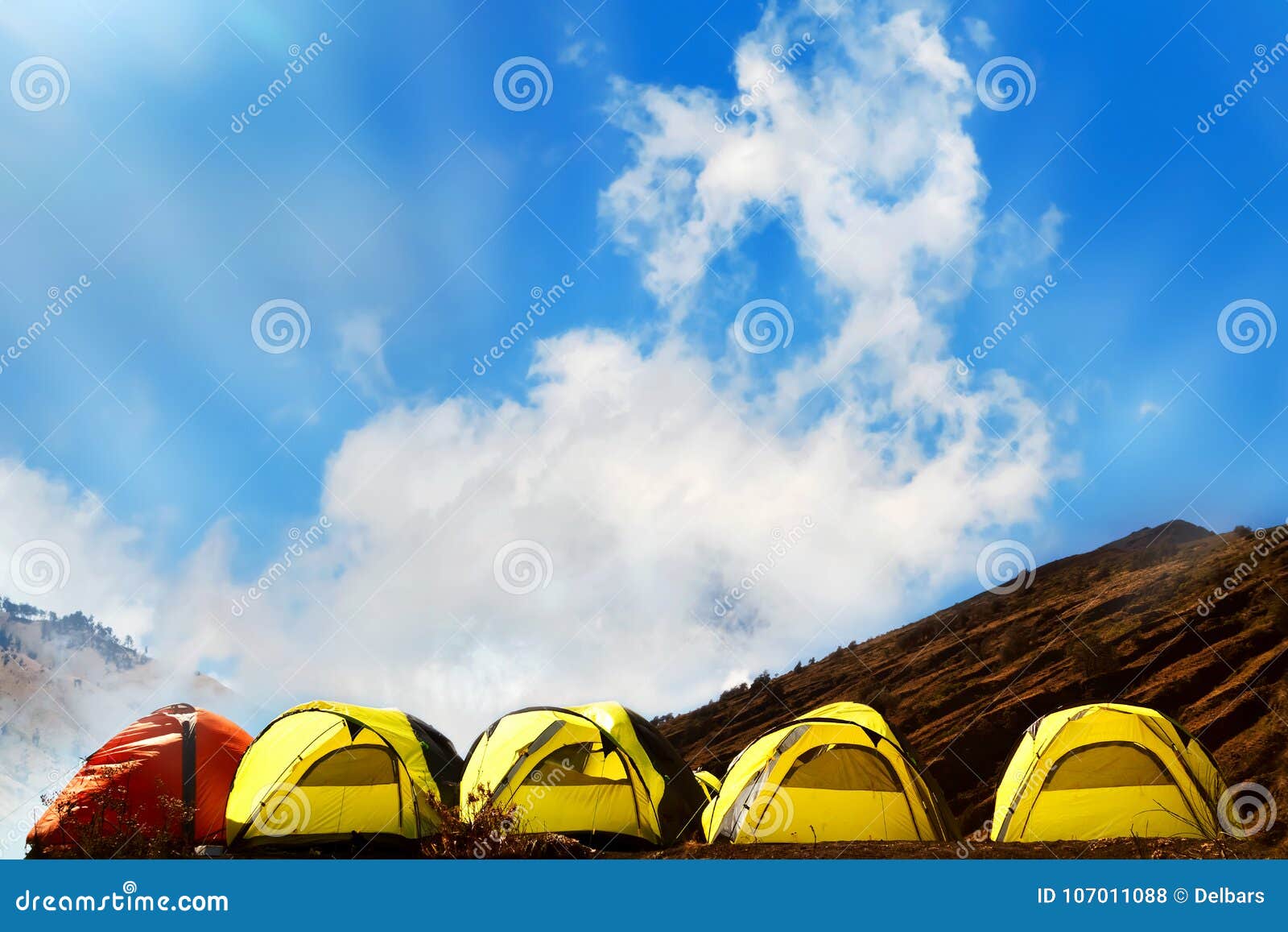 campground in the mountains. many yellow adn red tents against the blue sky with amazing clouds