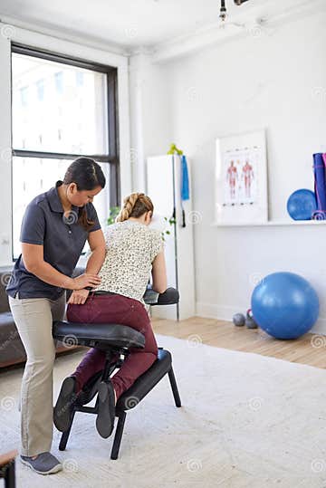 Chinese Woman Massage Therapist Giving A Neck And Back Pressure Treatment To An Attractive Blond