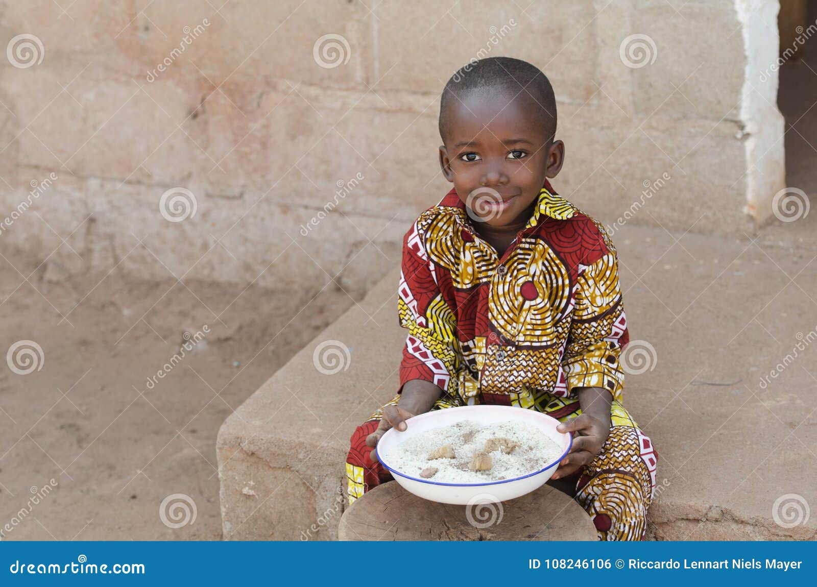 candid shot of little black african boy eating rice outdoors