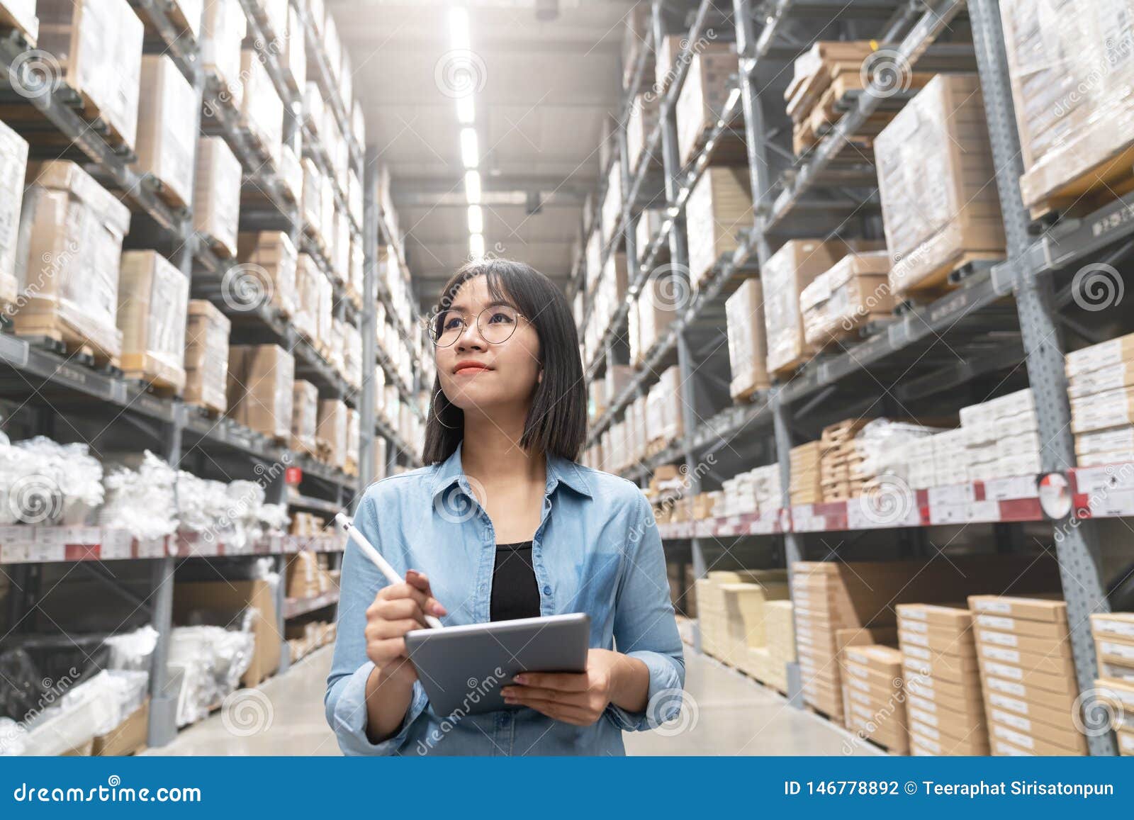 candid of young attractive asian woman auditor or trainee staff work looking up stocktaking inventory in warehouse store by