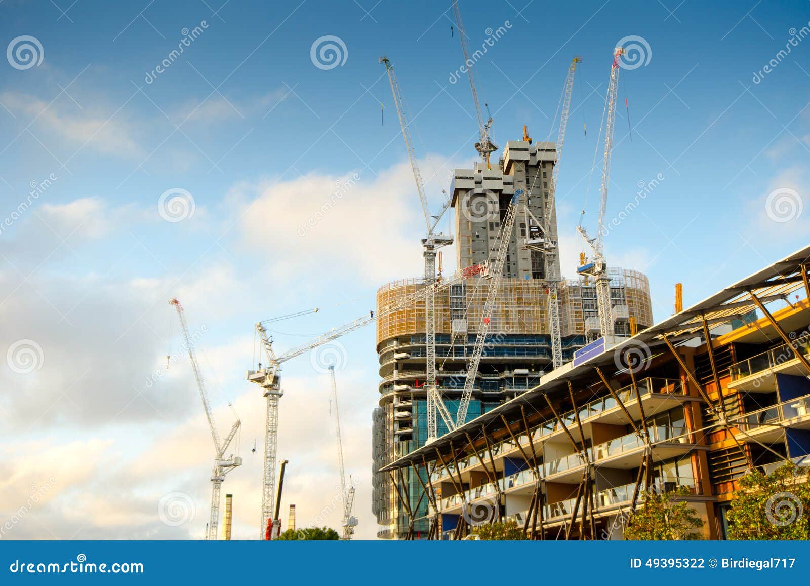 Canteiro de obras do Highrise com o céu azul nebuloso. Canteiro de obras do Highrise com muitos guindastes de levantamento, e fundo nebuloso do céu azul