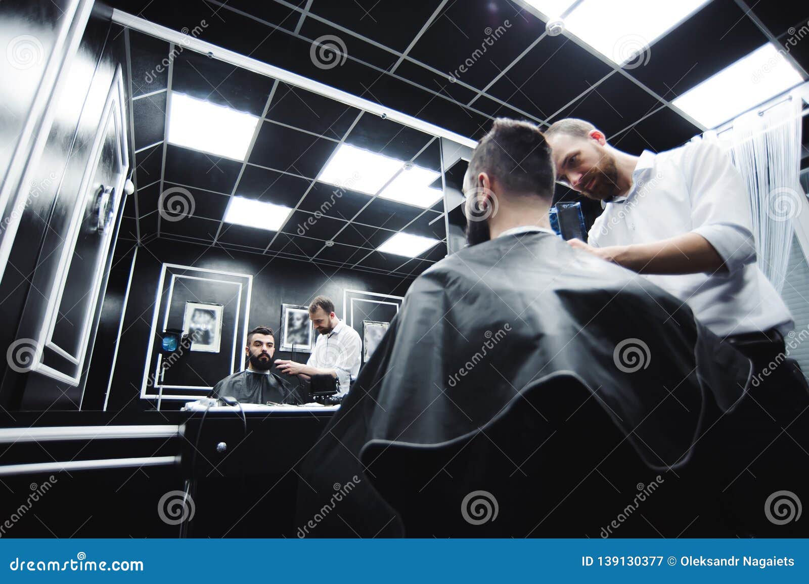 Capelli dei tagli e barba matrici degli uomini nel parrucchiere, parrucchiere. Il Master taglia i capelli e la barba degli uomini nel parrucchiere, parrucchiere fa l'acconciatura per un giovane