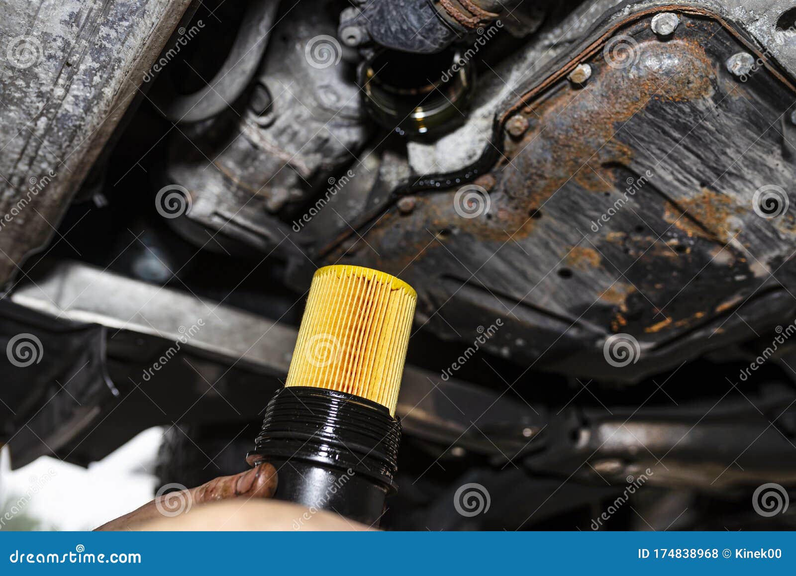 The Car Mechanic Screws a New Oil Filter on the Bottom of the Engine