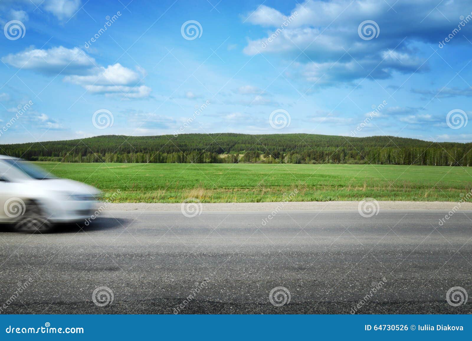 the car speeds along a country road, surrounded by forest and blue sky