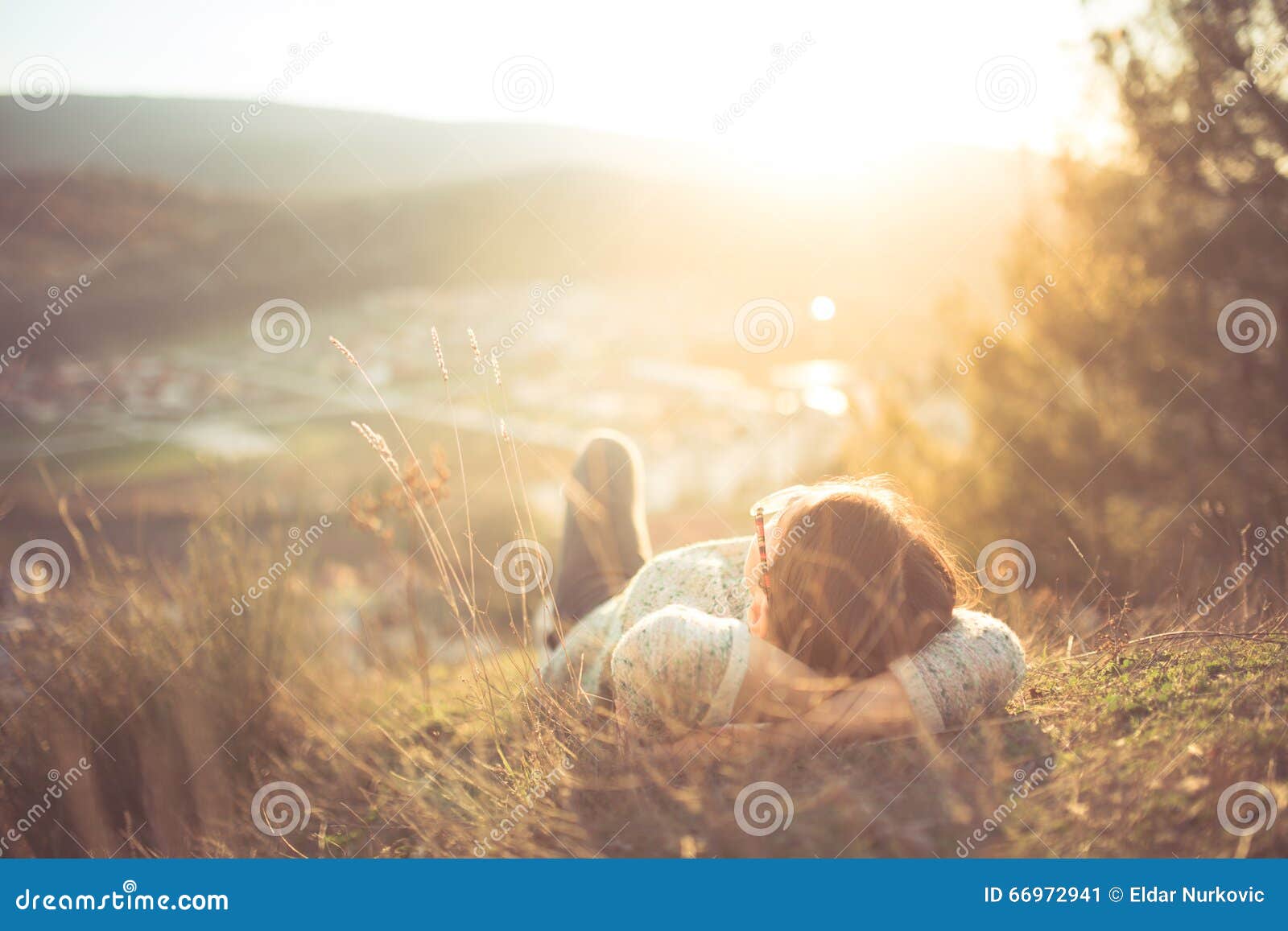 carefree happy woman lying on green grass meadow on top of mountain edge cliff enjoying sun on her face. enjoying nature sunset